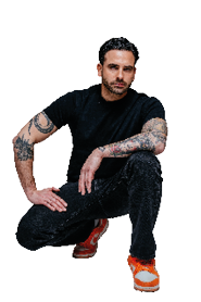 DJ Agatino Romero tr gt ein schwarzes T-Shirt, Jeans und Sneaker. Er hockt l ssig am Boden und schaut nach vorne.