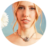 Die S ngerin LEA schaut frontal in die Kamera. Die blonde Frau tr gt eine hellgoldene Kette mit einem Bl ten-Amulett in der Mitte. Im Hintergrund ist eine halbe wei e Blume zu sehen.