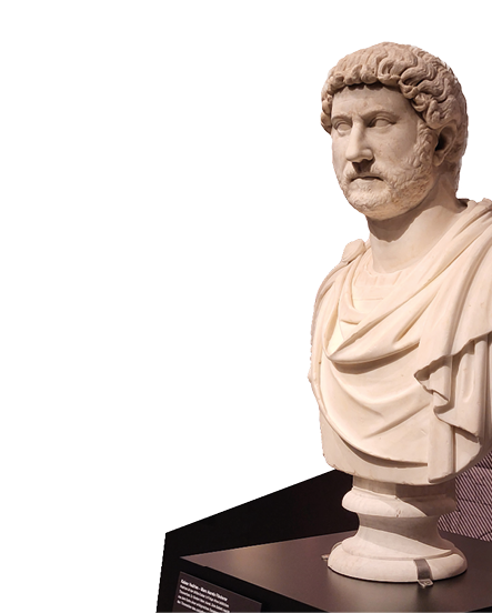 Das Bild zeigt eine antike, marmorne B ste eines r mischen Kaisers. Die B ste ist detailliert und realistisch gearbeitet. Der Kaiser tr gt eine Toga, die ber seine Schultern f llt, und hat einen ernsten Gesichtsausdruck. Sein Haar ist in lockigen Str hnen modelliert und bildet eine dichte, wellige M hne. Der Bart ist kurz und gepflegt. Die B ste ist auf einem Sockel aus schwarzem Material befestigt. 