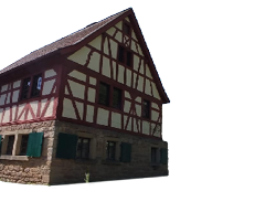 Das Bild zeigt eine l ndliche Szene bei strahlendem Sonnenschein und klarem, blauem Himmel. Im Mittelpunkt steht ein gut erhaltenes Fachwerkhaus mit auff lliger roter und wei er Balkenkonstruktion. Das Erdgeschoss besteht aus grob behauenem Naturstein, w hrend das Obergeschoss mit typischem Fachwerk gestaltet ist. Die Fensterl den im unteren Bereich des Hauses sind gr n gestrichen. Das Dach ist mit roten Ziegeln gedeckt und steil geneigt.   Links daneben ist ein weiteres Fachwerkgeb ude zu erkennen, das teilweise im Schatten liegt. Im Vordergrund erstreckt sich eine gepflasterte Fl che aus unregelm  igen Natursteinen.    Rechts im Bild, auf einem groben Holztisch oder einer Holzplattform, stehen zwei silberfarbene Milchkannen aus Metall. Die Perspektive ist leicht verzerrt durch den Weitwinkel, wodurch die Milchkannen im Verh ltnis gro  und dominant wirken. Aus einem Spalt im Holz w chst ein einzelner gr ner Grashalm hervor.    Im Hintergrund auf der rechten Seite sind weitere B ume, Wiesen mit gelben Bl ten und ein kleiner Holzzaun zu sehen, was die l ndliche und idyllische Atmosph re der Szene unterstreicht. Das Bild vermittelt Ruhe, Authentizit t und l ndliches Leben in einer vergangenen Zeit.