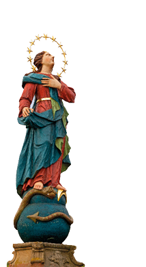 Das Bild zeigt eine bemalte Statue die auf einem Sockel steht. Die Figur tr gt ein langes, rotes Gewand mit einem blauen Mantel und einem gr nen Tuch. Um die Taille tr gt sie einen goldenen G rtel. Ihr rechter Fu steht auf einer blauen Kugel, um die sich eine Schlange mit einem Pfeil am Schwanz windet, w hrend ihr linker Fu  auf der Kugel ruht. Die Heilige hat eine goldene Krone aus Sternen um ihren Kopf, die wie ein Heiligenschein wirkt. Ihr Blick ist erhoben, die rechte Hand liegt auf ihrer Brust, die linke Hand h lt den blauen Mantel. Im Hintergrund sind unscharf Weinreben und H gel zu sehen, die von Herbstlaub in warmen Gelb- und Oranget nen umgeben sind. Der Himmel ist wolkig und wirkt leicht neblig.