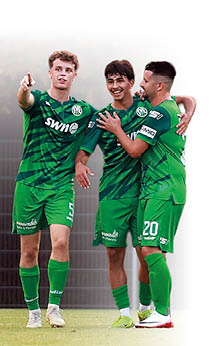 Drei junge M nner in gr nen Fu balltrikots feiern gemeinsam auf einem Fu ballplatz.   Alle drei Spieler tragen das gleiche gr ne Trikot mit dunkelgr nen diagonalen Streifen, der Aufschrift „swn“ auf der Brust sowie wei en R ckennummern.    Der Spieler ganz links zeigt mit dem rechten Arm gestikulierend nach vorne. Er wirkt energiegeladen und entschlossen.  Der mittlere Spieler l chelt breit und legt seinen Arm um den rechten Spieler. Er scheint sich sehr zu freuen.  Der rechte Spieler hat ebenfalls seinen Arm um den Mittleren gelegt. Auch er l chelt und wirkt zufrieden.    Alle drei tragen gr ne Shorts und lange gr ne Stutzen mit Fu ballschuhen. Sie stehen auf einem Rasenplatz.  Im Hintergrund ist ein dunkler Zaun zu erkennen, der in einem Unsch rfebereich liegt.    Die Szene zeigt einen emotionalen Moment der Freude – wahrscheinlich nach einem erfolgreichen Spielzug oder einem Tor. Sie vermittelt Teamgeist, Freundschaft und Zusammenhalt.