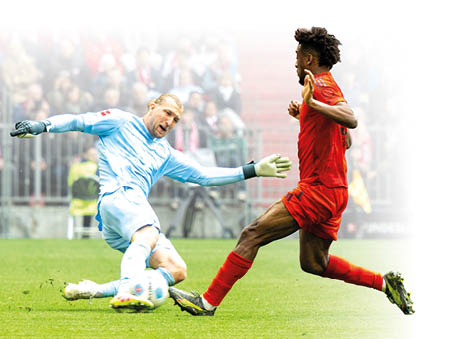 Auf dem Bild sieht man eine spannende Fu ballszene. Ein Torwart in hellblauer Kleidung rutscht auf dem Boden, um den Ball zu stoppen. Ihm gegen ber l uft ein Spieler in rotem Trikot und roten Hosen mit hoher Geschwindigkeit auf ihn zu. Beide sind mitten in der Aktion, ihre Bewegungen wirken kraftvoll und schnell. Im Hintergrund sind viele Zuschauer im Stadion zu sehen, die das Spiel verfolgen. Die Stimmung ist angespannt und dynamisch – es scheint ein wichtiger Moment im Spiel zu sein.