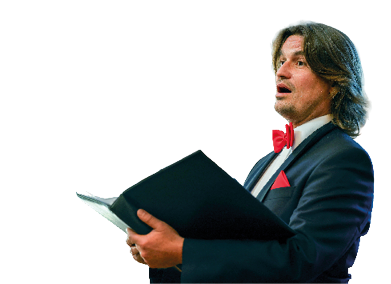 Ein S nger der Mainzer Hofs nger ist im Halbprofil zu sehen. Er tr gt einen schwarzen Anzug mit wei em Hemd, roter Fliege und rotem Einstecktuch. In den H nden h lt er eine schwarze Mappe mit Noten und singt konzentriert. Im Hintergrund sind weitere Chormitglieder unscharf erkennbar, ebenfalls in Anz gen mit roten Fliegen.