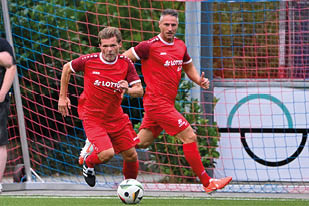 Das Bild zeigt eine gro e Gruppe fr hlicher Menschen auf einem Sportplatz. Sie haben sich zur bergabe eines symbolischen Spendenschecks von 10.000 € versammelt, gestiftet von LOTTO Rheinland-Pfalz.    Im Vordergrund steht ein gelbes „LOTTO Elf“-Schild. In der Mitte wird der Scheck hochgehalten – die Spende geht an ein Projekt zur Unterst tzung von Waisenkindern in Ruanda, wie aus der Aufschrift hervorgeht.    Die Gruppe besteht aus Sportlern (erkennbar an den roten „LOTTO Elf“-Trikots), Organisatoren, Unterst tzern und G sten – teils in Alltagskleidung, teils in thematisch passenden Shirts (z. B. „Rwanda“). Die Stimmung ist herzlich, engagiert und gemeinschaftlich – ein starkes Zeichen f r soziales Engagement durch Sport.