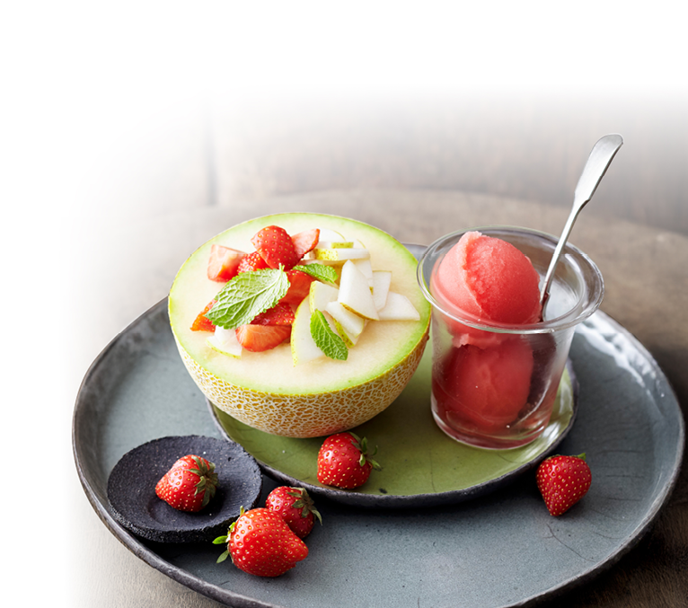 Halbe Honigmelone mit Fr chten gef llt, daneben Glas mit rotem Sorbet und Erdbeeren als Dekoration.