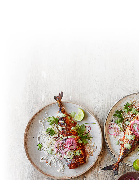 Zwei Teller mit gegrilltem Fisch auf Reis, garniert mit Kr uterso e, roten Zwiebeln, Koriander und Limetten.