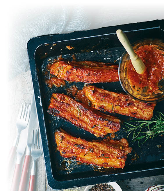 Gegrillte Schweinerippchen auf einem Blech, glasiert mit w rziger Marinade und Kr utern.