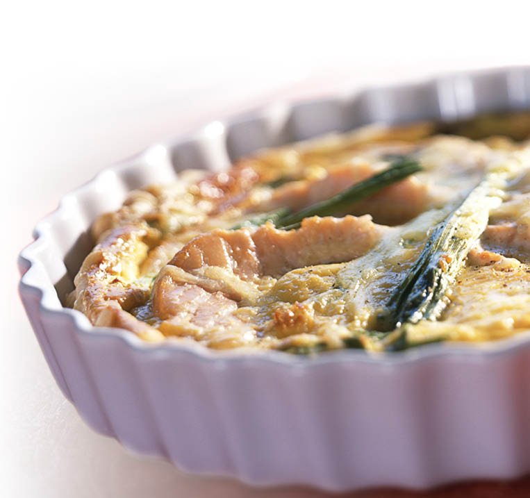 Frisch gebackene Quiche mit Gem se und Lachsst cken in wei er Backform.