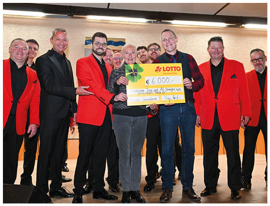 Im Rahmen einer feierlichen Veranstaltung berreichte Lotto Rheinland-Pfalz einen symbolischen Spendenscheck  ber 5.000 Euro. Mehrere M nner in auff lligen roten Sakkos, die Mainzer Hofs nger, versammelten sich gemeinsam mit Vertretern von Lotto Rheinland-Pfalz f r das Erinnerungsfoto. Strahlend hielten sie den gro en gelben Scheck in die Kamera. Die Spende kommt einem gemeinn tzigen Zweck zugute und unterstreicht das soziale Engagement des Unternehmens, das sich regelm  ig f r kulturelle und soziale Projekte in der Region einsetzt. Die Atmosph re war herzlich und von sp rbarer Freude  ber die Unterst tzung gepr gt.
