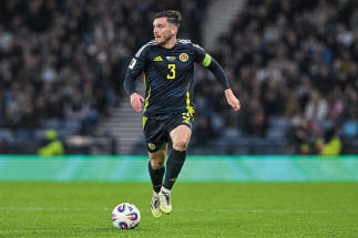 Fu ballspieler in schwarzem Trikot mit gelben Details und Kapit nsbinde l uft mit Ball auf gr nem Spielfeld.