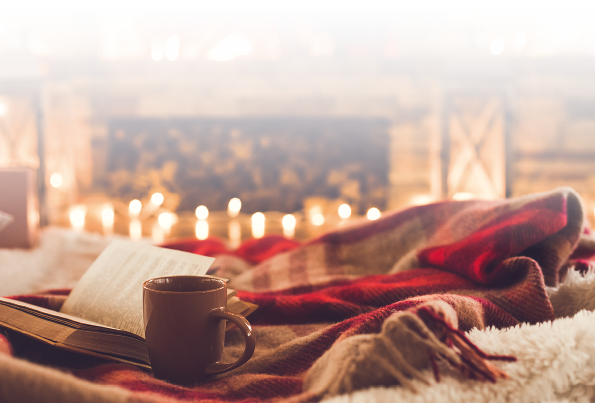 Das Bild zeigt eine gem tliche, warme Szene: Im Vordergrund liegen eine aufgeschlagene Buchseite und eine Tasse – vermutlich mit Tee, Kakao oder Kaffee – auf einer weichen, rot-karierte Decke.  Im Hintergrund brennen zahlreiche Kerzen, deren weiches Licht f r eine stimmungsvolle Atmosph re sorgt.    Die Szene vermittelt ein Gef hl von Geborgenheit, Entspannung und Wintergem tlichkeit – perfekt f r einen ruhigen Abend am Kamin mit einem guten Buch.