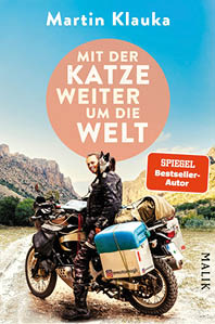 Das Bild zeigt das Buchcover von „Mit der Katze weiter um die Welt“ von Martin Klauka, erschienen im Malik Verlag. Das Cover zeigt den Autor auf einem Motorrad, beladen mit Reisegep ck, in einer felsigen Landschaft mit Bergen und blauem Himmel im Hintergrund. Auf seiner Schulter sitzt eine schwarz-wei e Katze, die aufmerksam in die Ferne blickt – sie ist ein zentraler Blickfang des Motivs.  Der Titel steht in gro en wei en Buchstaben in einem orangefarbenen Kreis vor dem Himmel:  „Mit der Katze weiter um die Welt“.  Rechts unten befindet sich ein rotes Label mit der Aufschrift „SPIEGEL Bestseller-Autor“.  Das Bild vermittelt Abenteuerlust, Freiheit und eine besondere Mensch-Tier-Bindung – passend zu einem Reisebericht voller Erlebnisse und Emotionen.