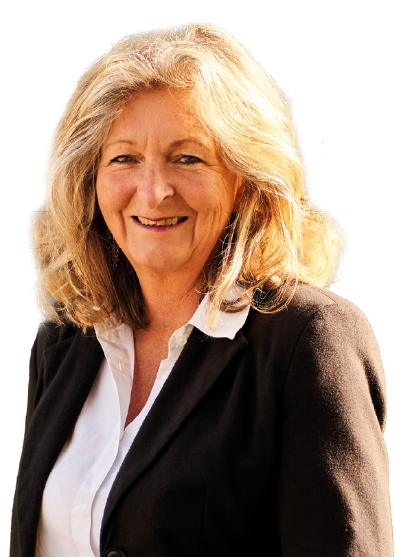 Frau mit schulterlangem, gewelltem, blondem Haar tr gt wei e Bluse und schwarzen Blazer, steht im Freien vor unscharfem Hintergrund mit B umen.