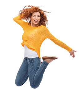 Frau mit freudigem Gesichtsausdruck springt mit nach hinten angwinkelten Beinen vor Freude in die Luft