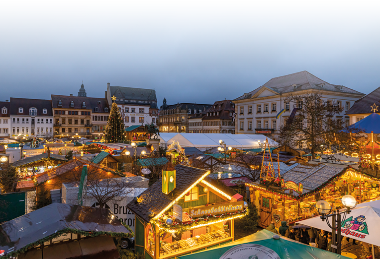 Das Bild zeigt den kunsthandwerklichen Thomas-Nast-Nikolausmarkt in weihnachtlichem Glanz. Zahlreiche festlich geschm ckte Buden reihen sich aneinander und verbreiten warmes Licht in der winterlichen Abendstimmung. In der Mitte des Marktplatzes steht ein gro er, hell erleuchteter Weihnachtsbaum, der von historischen Geb uden umrahmt wird. Besucherinnen und Besucher schlendern zwischen den St nden, genie en die Atmosph re und das vielf ltige Angebot aus Kunsthandwerk, Leckereien und Geschenkideen – ein stimmungsvoller Ort, der Weihnachtsfreude und Tradition miteinander verbindet.