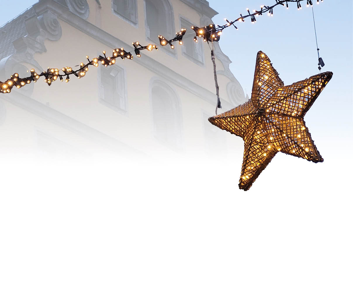 Ein leuchtender Stern einer Weihnachtsmarktbeleuchtung h ngt vor einer barocken Hausfassade.