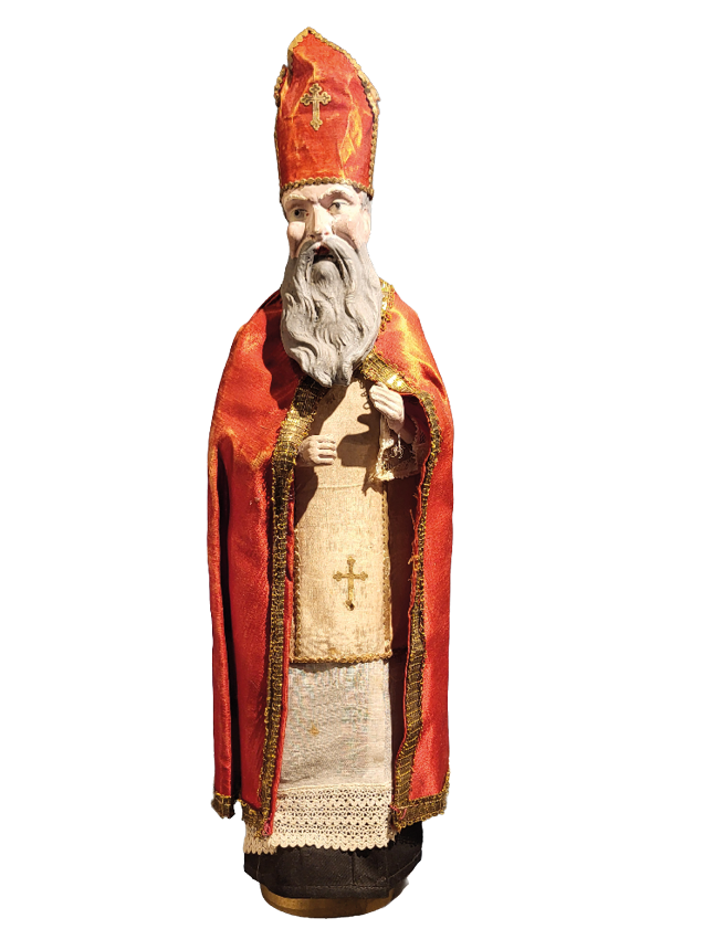 Auf dem Bild ist eine Figur des Heiligen Nikolaus zu sehen. Die Merkmale sprechen klar daf r: Er tr gt eine rote Mitra (Bischofshaube) mit einem goldenen Kreuz. Ein langen grauen Bart, wie er typischerweise bei Darstellungen des Nikolaus vorkommt. Ein rotes Bischofsgewand mit goldenen Verzierungen und eine reich gestaltete Stola.    In der Hand h lt er etwas, das wie ein kleines Buch oder eine Bibel wirkt – ein weiteres typisches Attribut kirchlicher Figuren. Die Figur scheint handgefertigt und historisch oder im Stil alter Volkskunst gestaltet zu sein – m glicherweise ein Teil einer Krippen- oder Weihnachtsdarstellung.