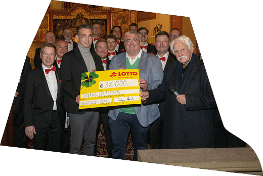 Im festlichen Ambiente einer Kirche berreichte Lotto Rheinland-Pfalz einen Spendenscheck an die Vertreterinnen und Vertreter der Empf ngerorganisation. Gemeinsam mit den Mitgliedern der Mainzer Hofs nger, die in eleganten schwarzen Anz gen mit roten Fliegen erschienen waren, wurde die  bergabe feierlich begangen. Das Gruppenfoto zeigt strahlende Gesichter und unterstreicht die Wertsch tzung f r das Engagement vor Ort – ein Moment, der Gemeinschaftsgef hl und gelebte Unterst tzung eindrucksvoll sichtbar macht.