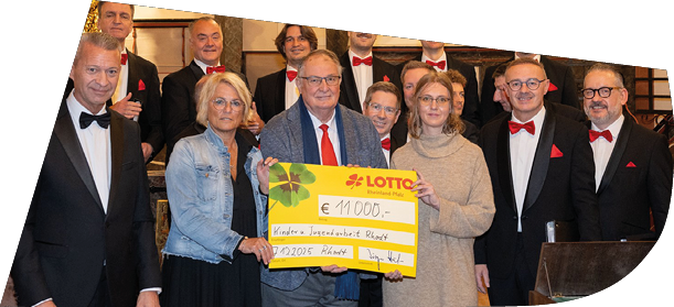Im festlichen Ambiente einer Kirche berreichte Lotto Rheinland-Pfalz einen Spendenscheck an die Vertreterinnen und Vertreter der Empf ngerorganisation. Gemeinsam mit den Mitgliedern der Mainzer Hofs nger, die in eleganten schwarzen Anz gen mit roten Fliegen erschienen waren, wurde die  bergabe feierlich begangen. Das Gruppenfoto zeigt strahlende Gesichter und unterstreicht die Wertsch tzung f r das Engagement vor Ort – ein Moment, der Gemeinschaftsgef hl und gelebte Unterst tzung eindrucksvoll sichtbar macht.
