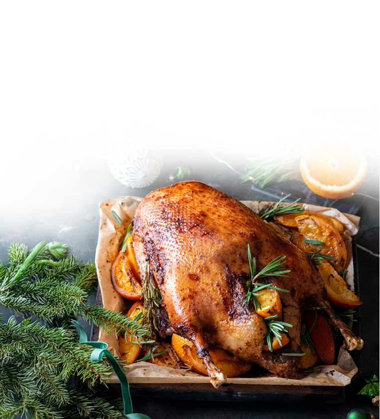 Gebratene Gans mit Orangenscheiben und Rosmarinzweigen auf Backpapier, umgeben von Tannenzweigen, Kerzen und Weihnachtskugeln.