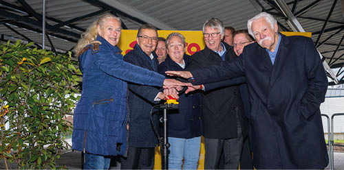 Eine Gruppe steht um einen roten Buzzer und halten jeeine Hand ber den Buzzer. Es scheint, als ob die Gruppe den Buzzer zusammen ausl sen m chte.   