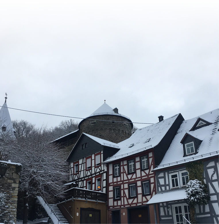 Das Foto zeigt den winterlichen historischen Ortskern von Herrstein mit sch n restaurierten Fachwerkh usern und einem markanten Rundturm aus Bruchstein, der ber den D chern aufragt. Die Szene wirkt sehr idyllisch und typisch f r alte Burg- oder Stadtanlagen im Westen Deutschlands.