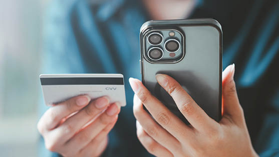 Auf dem Bild sind die H nde einer Person zu sehen, die gleichzeitig ein Smartphone und eine Kreditkarte h lt. Das Smartphone wird aufrecht gehalten, die R ckseite mit mehreren Kameralinsen ist sichtbar. In der anderen Hand befindet sich eine helle Kreditkarte.