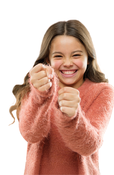 Ein junges M dchen steht frontal zur Kamera. Sie l chelt breit und zeigt ihre Z hne, ihre Augen sind vor Freude leicht zusammengekniffen. Beide H nde sind vor dem K rper zu F usten geballt und nach vorne gestreckt, als w rde sie sich freuen oder etwas feiern. Sie tr gt einen lang rmeligen, flauschigen Pullover. Ihre langen Haare fallen locker ber die Schultern. Die K rperhaltung und der Gesichtsausdruck wirken sehr fr hlich und energiegeladen.