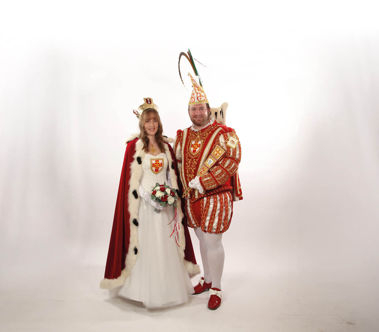 Ein Mann und eine Frau verkleidet als Karnevalsprinzenpaar in festlichen Kost men mit Umhang, Krone, Zepter und Blumenstrau vor wei em Hintergrund.
