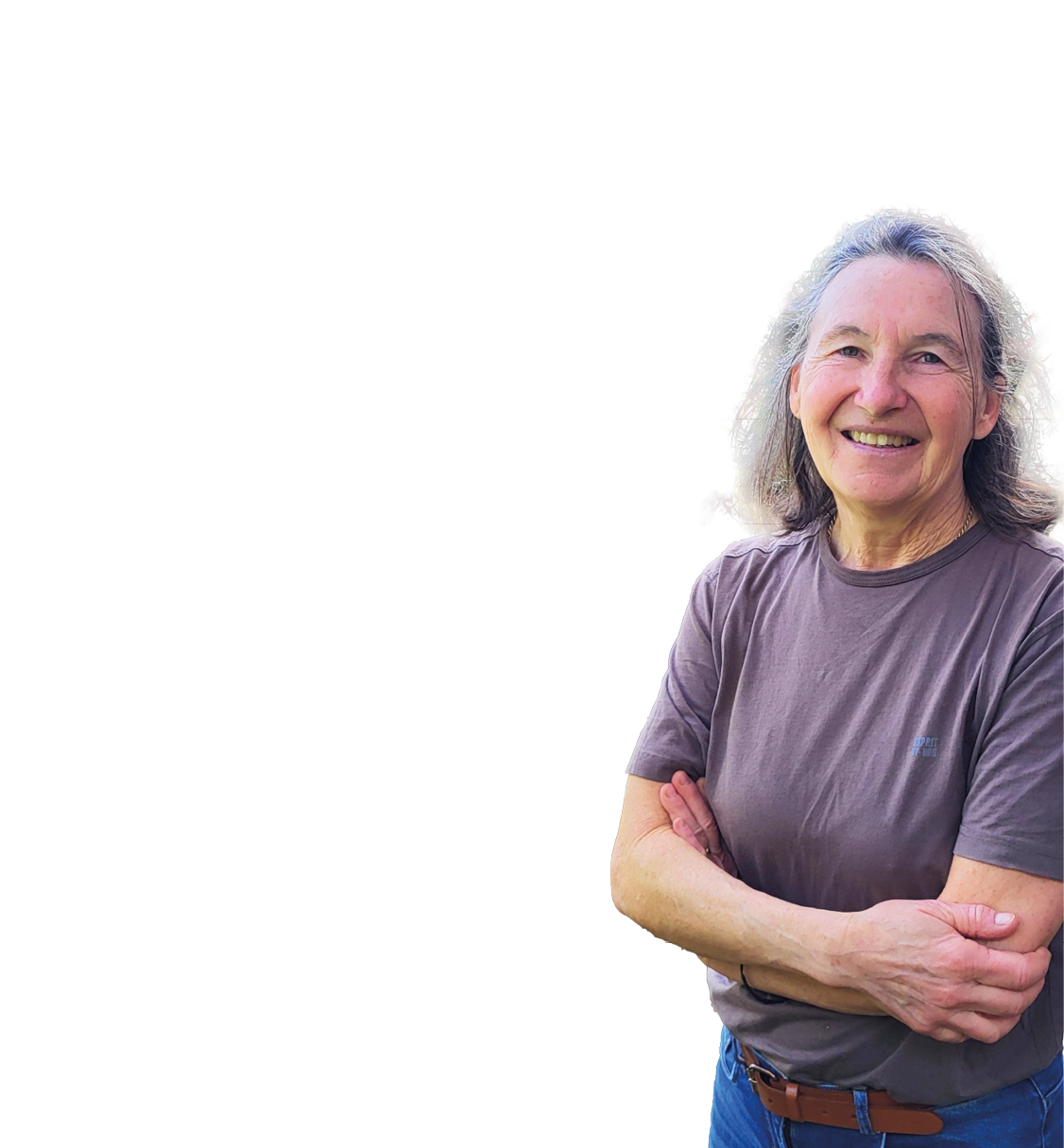 Frau mit grauen Haaren und braunem T-Shirt steht mit verschr nkten Armen vor einem Baum und einer h ngenden Korbschaukel auf einer Wiese mit B umen im Hintergrund