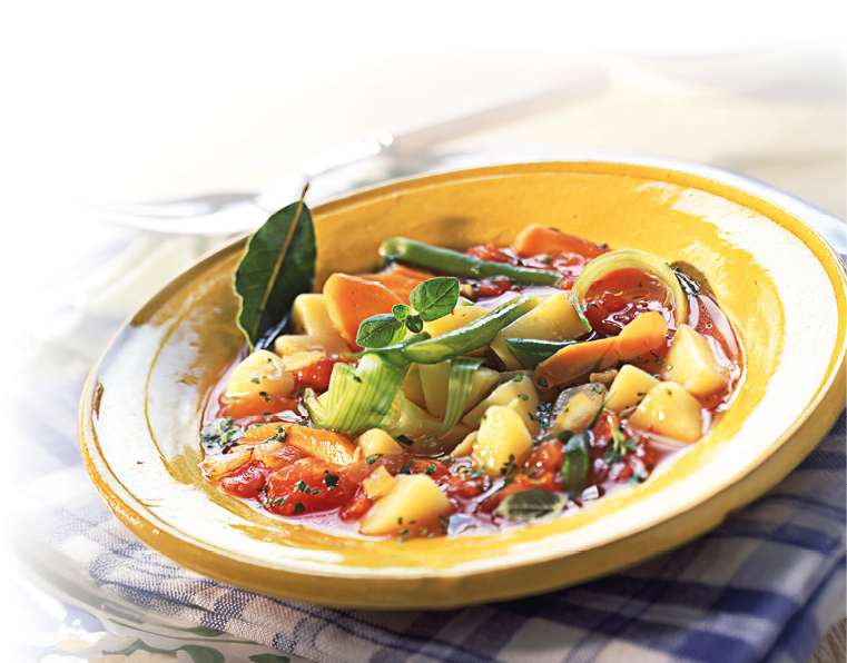 Zu sehen ist eine gelbe, flache Keramikschale mit einer klaren, r tlichen Gem sesuppe. In der Br he liegen gew rfelte Kartoffeln, Karottenscheiben, gr ne Bohnen und Tomatenst cke; dar ber sind frische Kr uter gestreut. Als Garnitur sind ein Lorbeerblatt sowie gr ne Streifen von Lauch oder Fr hlingszwiebel in der Mitte platziert. Die Schale steht auf einem blau-wei karierten Tuch; im hellen Hintergrund sind Teller und Besteck unscharf zu erkennen.