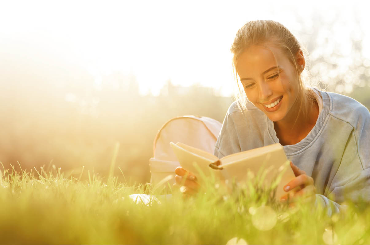 Eine Person liegt auf einer Wiese im Sonnenlicht und liest ein Buch, w hrend sie entspannt die Beine anhebt. Beschreibung von KI generiert