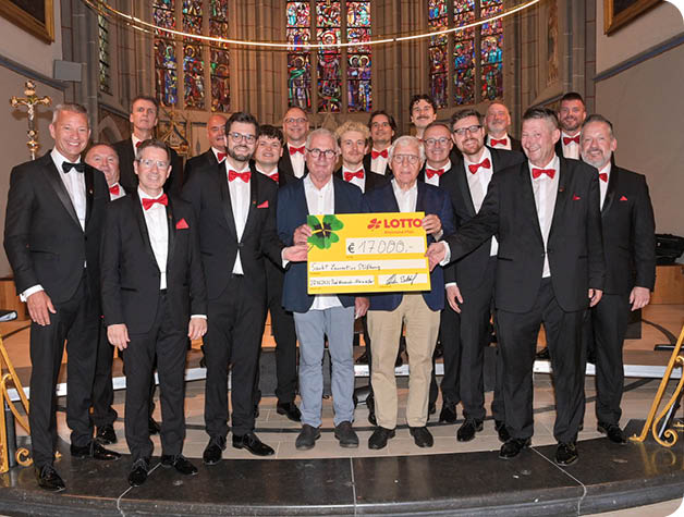 Eine Gruppe von Erwachsenen in formeller Kleidung steht in einer Kirche und h lt gemeinsam einen gro en symbolischen Scheck. Beschreibung von KI generiert