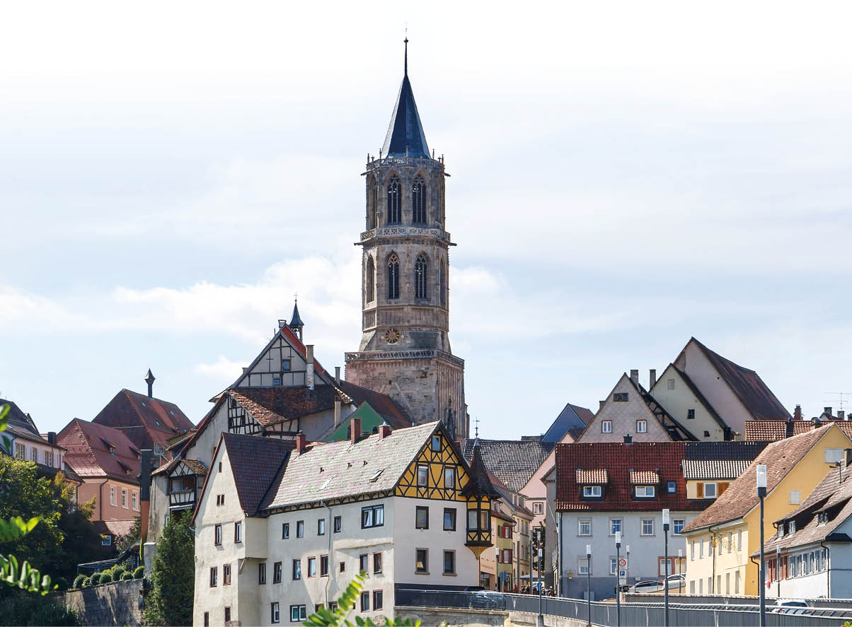 Eine historische Stadtansicht mit Fachwerkh usern und einem hohen Kirchturm unter einem bew lkten Himmel. Beschreibung von KI generiert