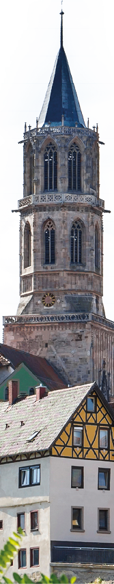 Eine historische Stadtansicht mit Fachwerkh usern und einem hohen Kirchturm im Hintergrund bei klarem Himmel. Beschreibung von KI generiert