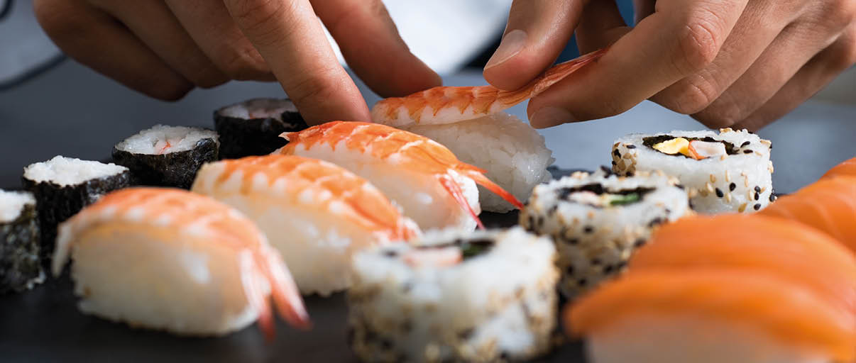Closeup of chef hands preparing japanese food. Japanese chef making sushi at restaurant. Young chef serving traditional japanese sushi served on a black stone plate.