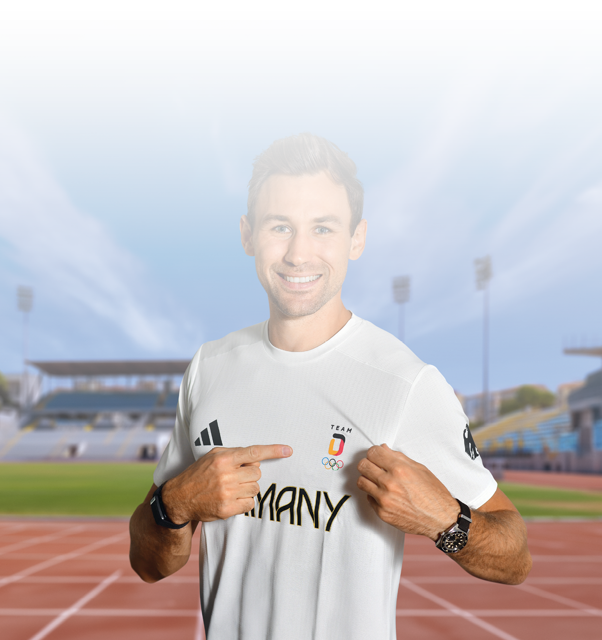 Eine l chelnde Person zeigt mit beiden H nden auf das wei e Trikot mit dem Schriftzug „Germany“ und dem Logo der Olympiamannschaft auf einer Laufbahn im Freien. Beschreibung von KI generiert