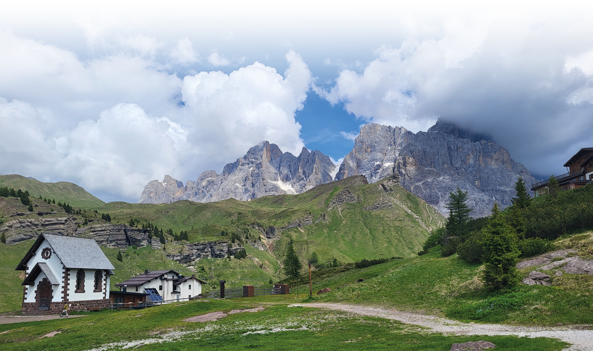 Kleine H user stehen auf einer gr nen Wiese vor einer Berglandschaft mit bew lktem Himmel. Beschreibung von KI generiert