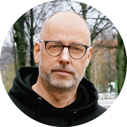 Eine Person mit Brille tr gt einen schwarzen Kapuzenpullover und hat einen kurzen grauen Bart. Beschreibung von KI generiert