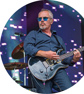 Eine Person tr gt ein blaues Hemd und spielt eine Gitarre vor einem dunklen Hintergrund. Beschreibung von KI generiert