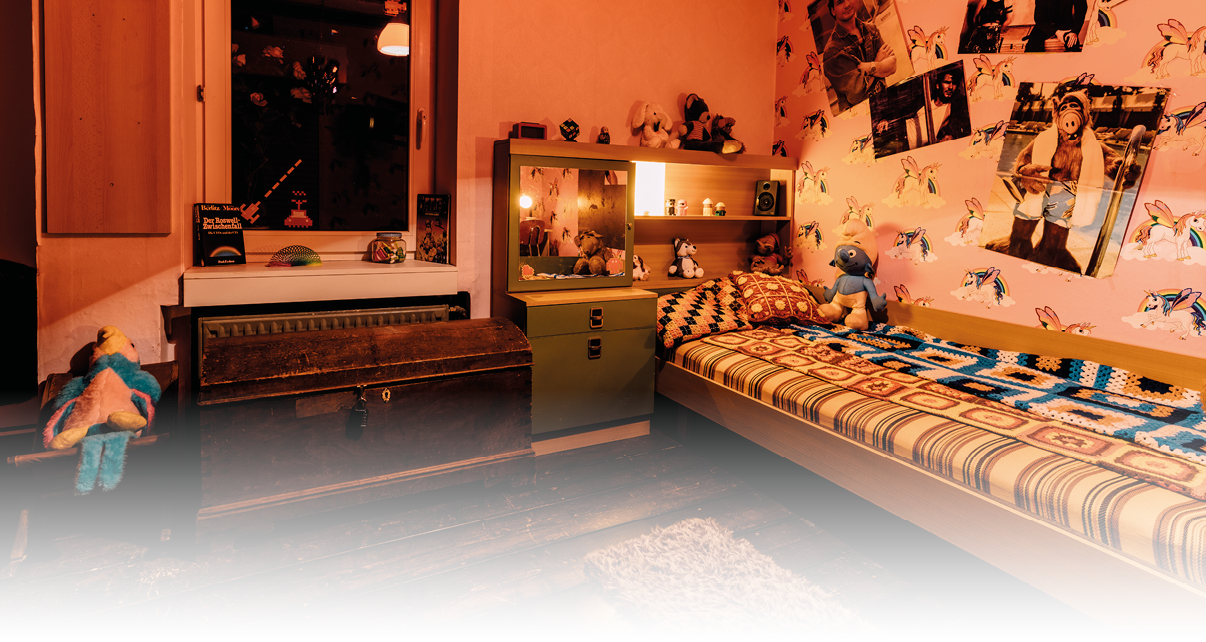 Ein gem tlich eingerichtetes Kinderzimmer mit einem Einzelbett, bunten Kuscheltieren, einer Truhe, einem kleinen Schrank und an der Wand befestigten Postern und Tapeten mit Tiermotiven. Beschreibung von KI generiert