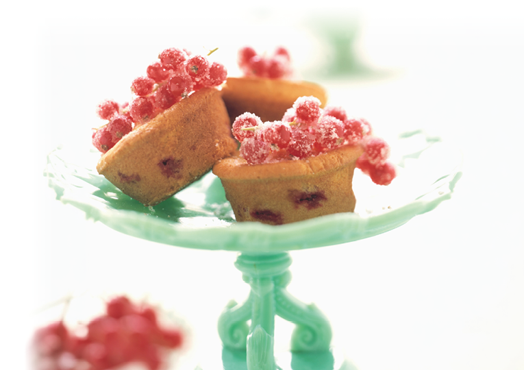 Drei kleine Kuchen mit roten Beeren stehen auf einem hellgr nen, verzierten Tortenst nder. Beschreibung von KI generiert