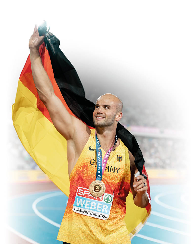 Eine Person tr gt ein Sporttrikot mit der Aufschrift Deutschland und h lt eine deutsche Flagge hinter sich, w hrend sie eine Medaille um den Hals tr gt und auf einer Laufbahn steht. Beschreibung von KI generiert