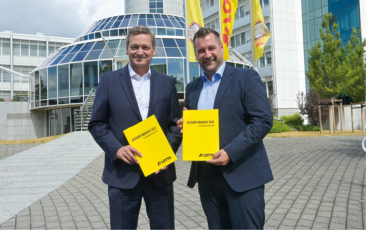 Zwei Personen in Anz gen halten l chelnd gelbe Ordner vor einem modernen Glasgeb ude mit Fahnen. Beschreibung von KI generiert