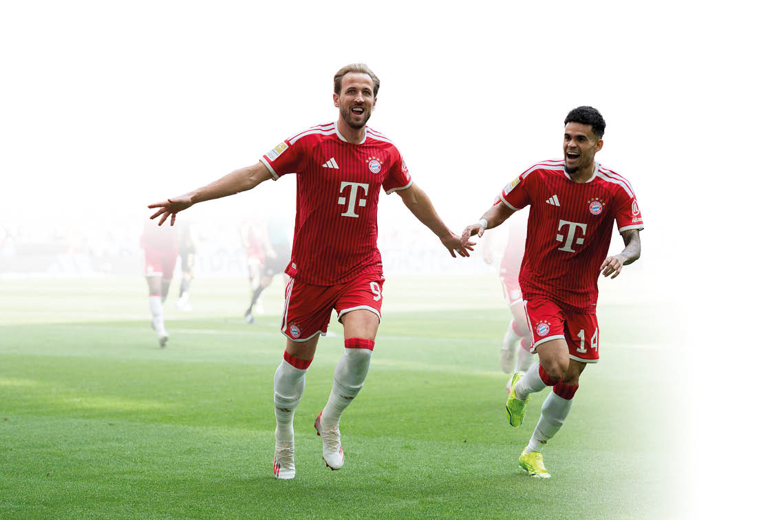 Zwei Erwachsene in roten Fu balltrikots laufen jubelnd auf einem Spielfeld, wobei sie sich an den H nden halten. Beschreibung von KI generiert
