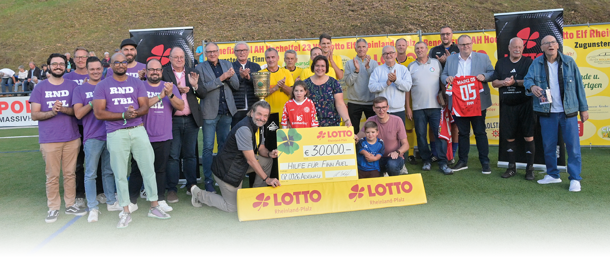 Eine Gruppe von Erwachsenen steht auf einem Sportfeld und pr sentiert gemeinsam einen gro en symbolischen Scheck mit Lotto-Logo vor einer Werbebande. Beschreibung von KI generiert