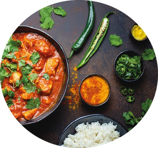 Ein Teller mit Reis, eine Sch ssel mit einem roten Currygericht garniert mit frischem Koriander, daneben gr ne Chilischoten, Gew rze und kleine Schalen mit weiteren Kr utern und So en auf dunklem Untergrund. Beschreibung von KI generiert