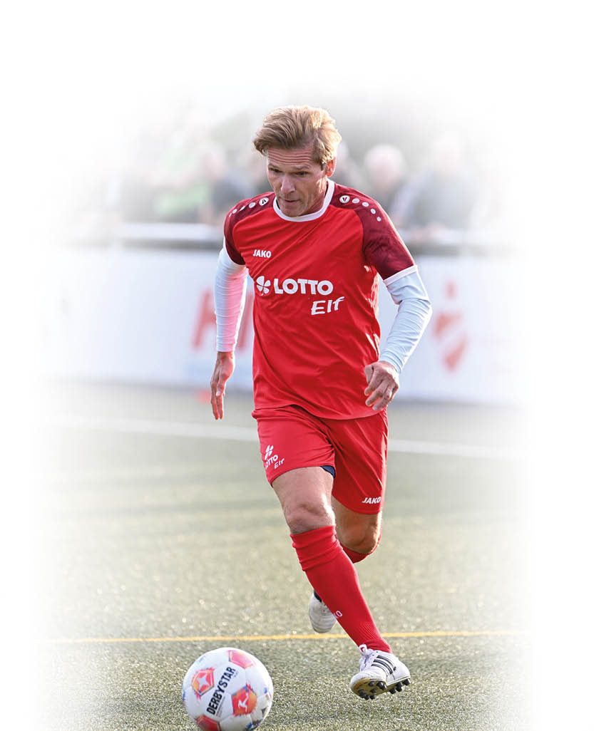 Eine Person mit rotem Sporttrikot und roten Shorts spielt Fu ball auf einem Spielfeld. Beschreibung von KI generiert