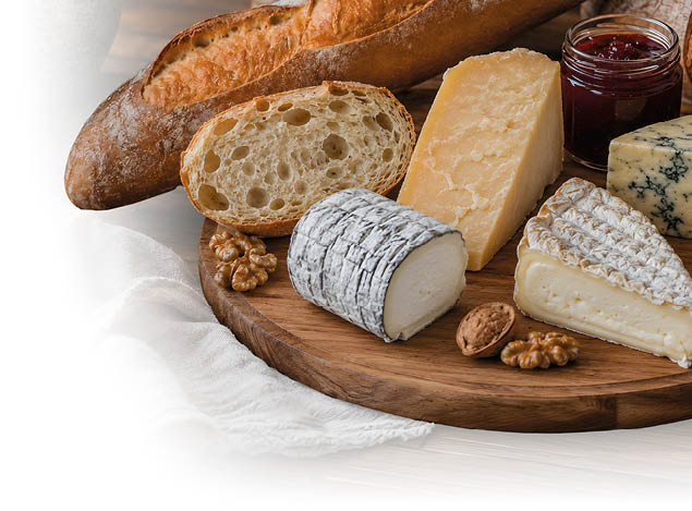 Verschiedene K sesorten, Baguette, Waln sse und ein Glas Marmelade sind auf einem runden Holzbrett auf einem Holztisch angerichtet. Beschreibung von KI generiert
